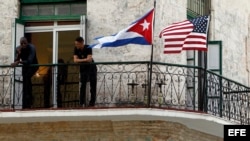 Dos jóvenes cubanos conversan junto a las banderas de Estados Unidos y Cuba en una vivienda de La Habana. 